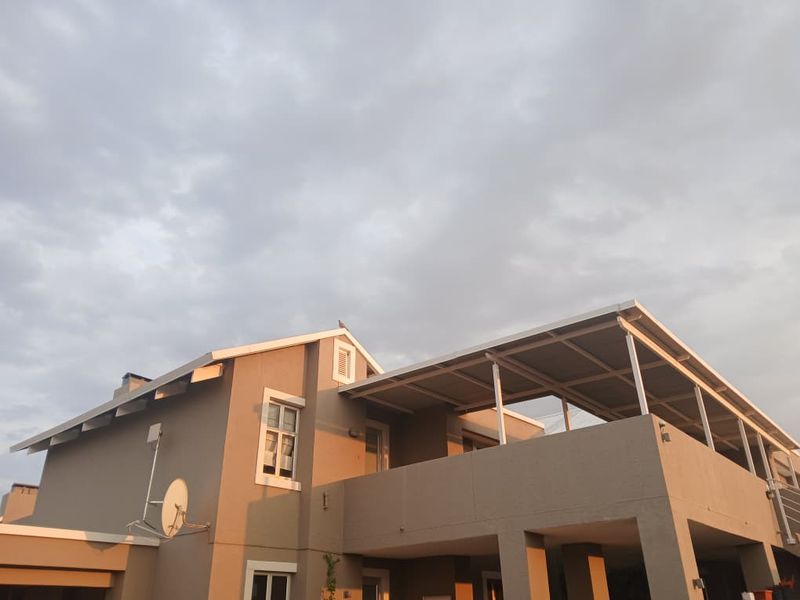 Rear elevation of the apartment building featuring a covered patio area and a pitched roof structure under a cloudy sky.