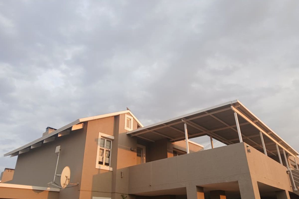 Rear elevation of the apartment building featuring a covered patio area and a pitched roof structure under a cloudy sky.