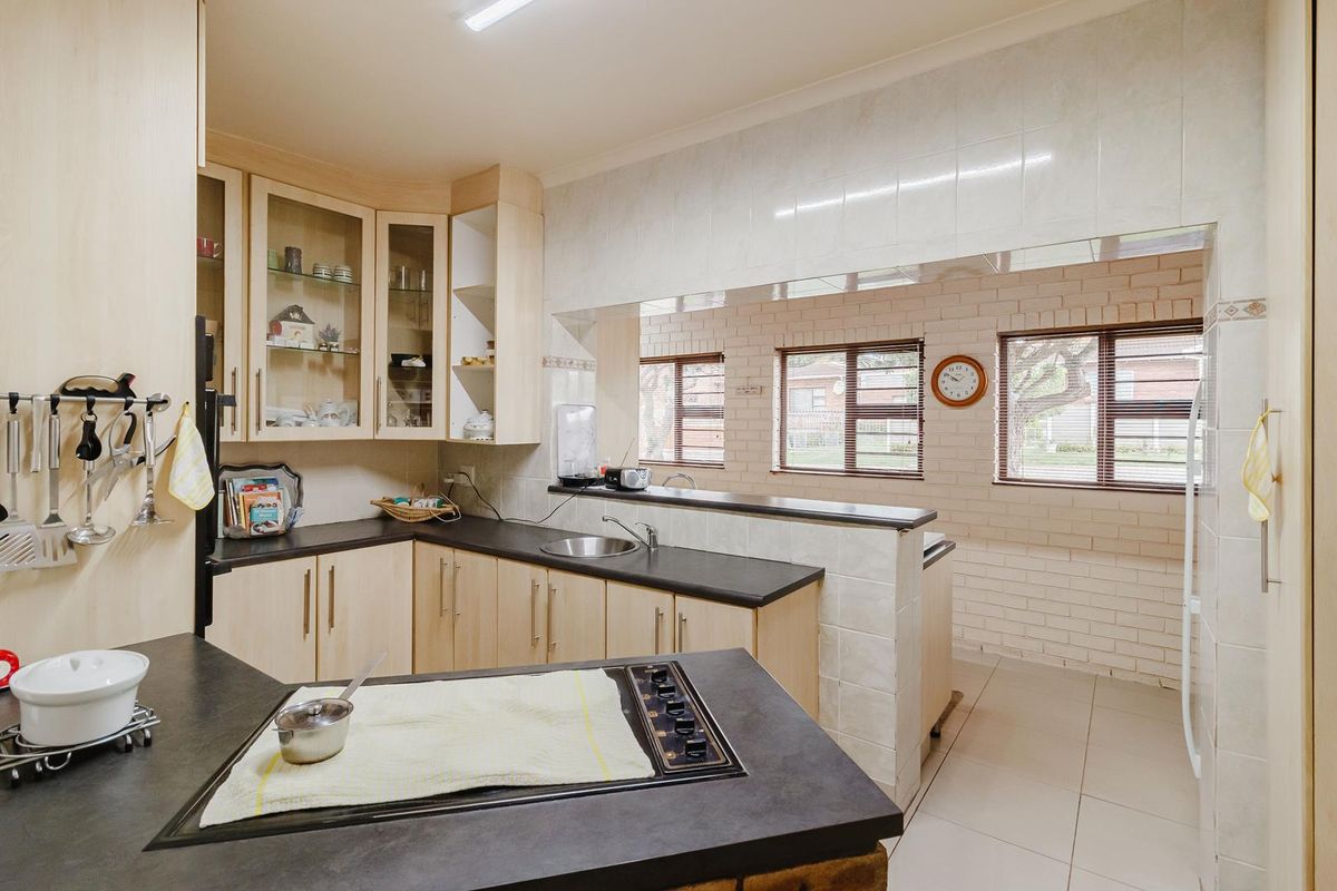 A functional kitchen featuring light wood-tone cabinetry, dark laminate countertops, a built-in hob, and a breakfast bar overlooking the adjacent living area.