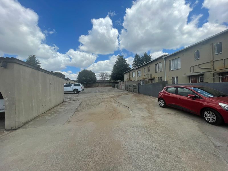 Rear exterior view of the townhouse complex featuring a shared concrete driveway and boundary walls with visible surface wear.