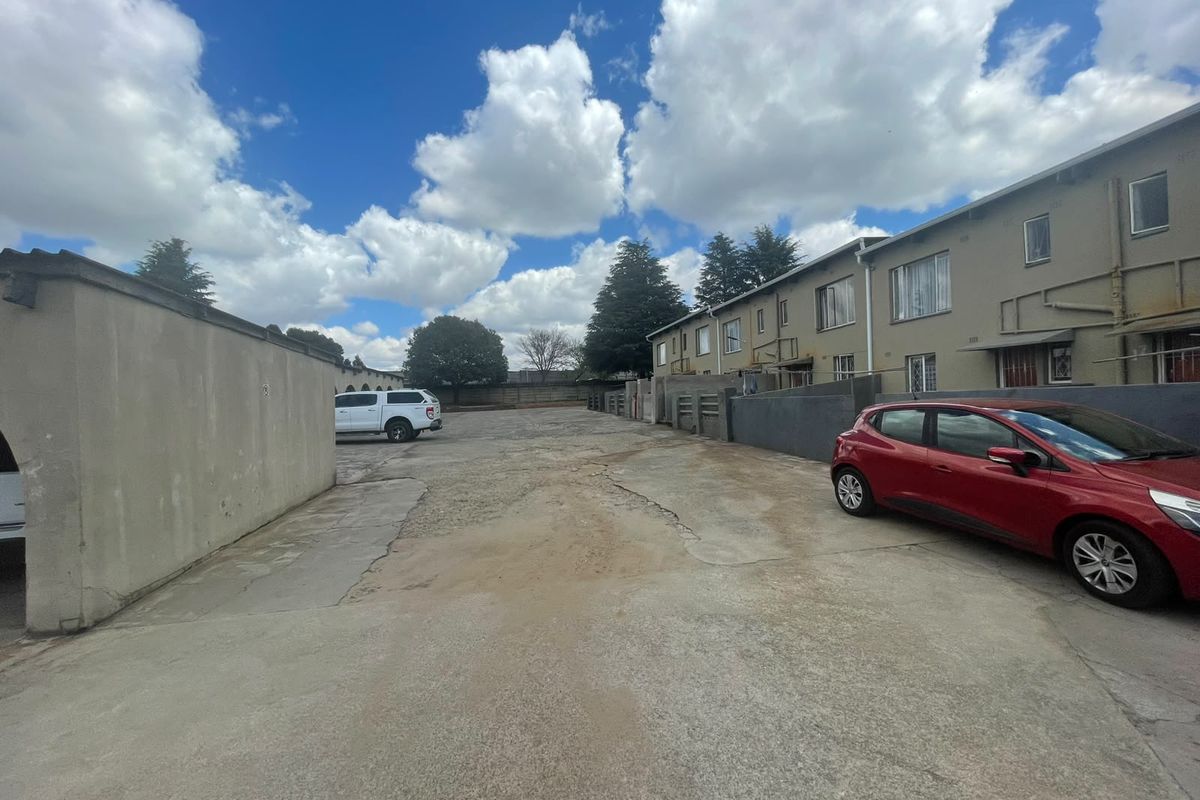Rear exterior view of the townhouse complex featuring a shared concrete driveway and boundary walls with visible surface wear.