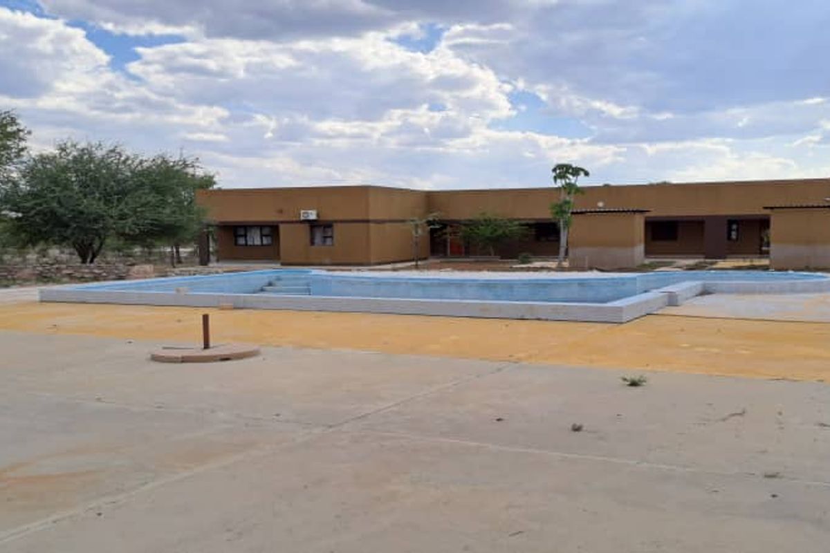 Outdoor pool area featuring a concrete deck and lodge building facade, requiring maintenance to the pool surround and exterior finishes.