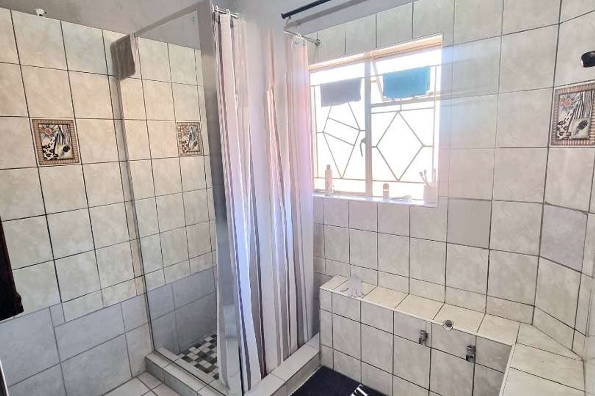 A functional bathroom featuring a tiled shower enclosure, a built-in tiled bathtub, and a window with security bars.