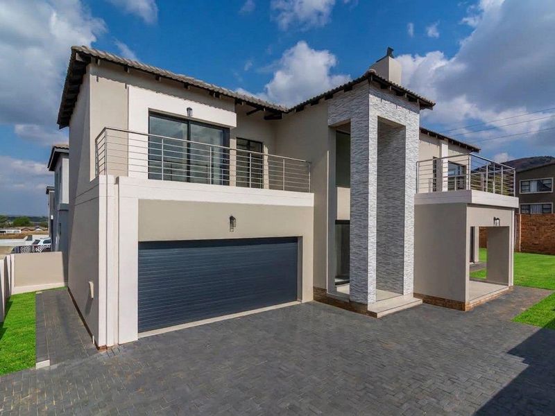 Modern double-story residence featuring a paved driveway, double garage, stone-clad entrance pillar, and upper-level balconies with stainless steel railings.