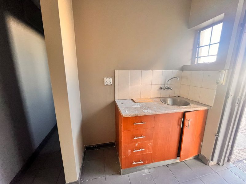 A compact kitchenette area featuring built-in cabinetry, a stainless steel sink, and tiled backsplash, suitable for a small office or retail utility space.