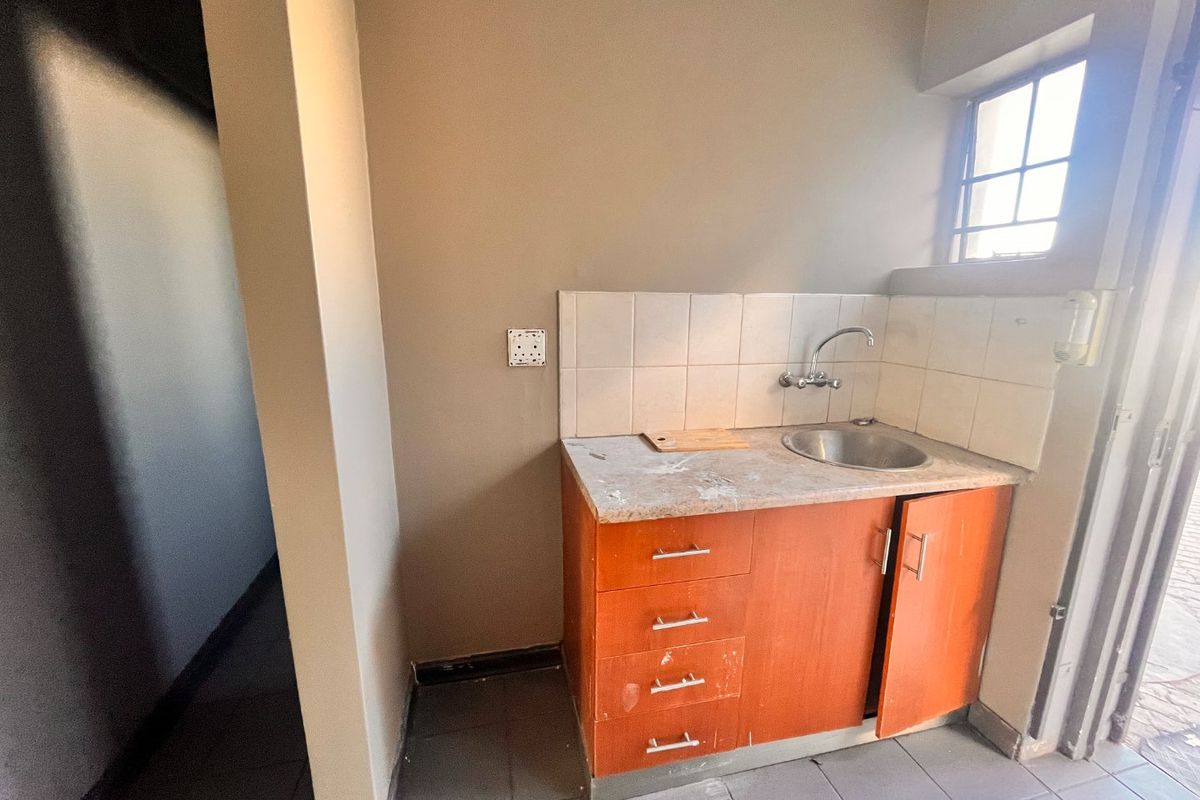 A compact kitchenette area featuring built-in cabinetry, a stainless steel sink, and tiled backsplash, suitable for a small office or retail utility space.