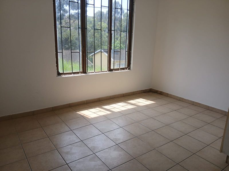 A bright, empty bedroom featuring neutral tiled flooring and large windows fitted with security bars, offering a clean canvas for personalization.