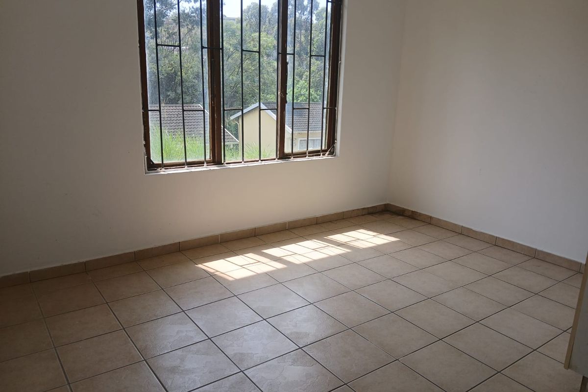 A bright, empty bedroom featuring neutral tiled flooring and large windows fitted with security bars, offering a clean canvas for personalization.