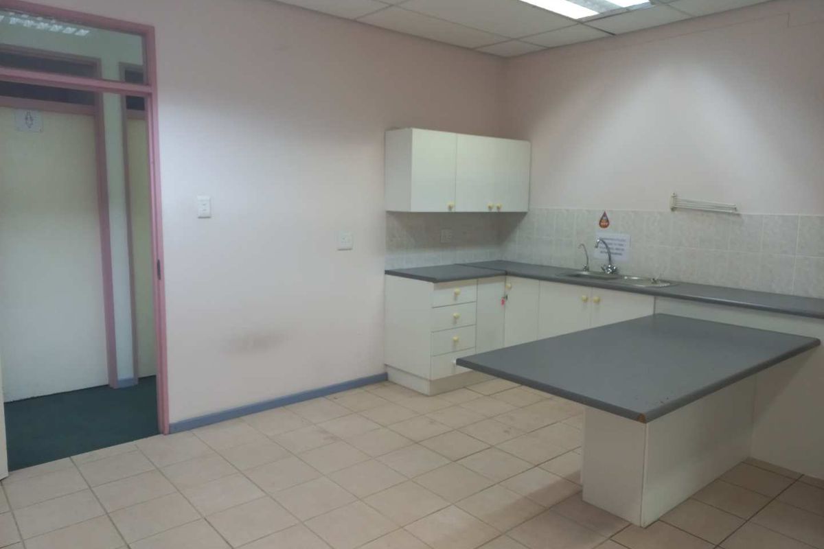 A functional office kitchenette featuring built-in cabinetry, laminate countertops, a stainless steel sink, and tiled flooring, providing a practical break area for staff.