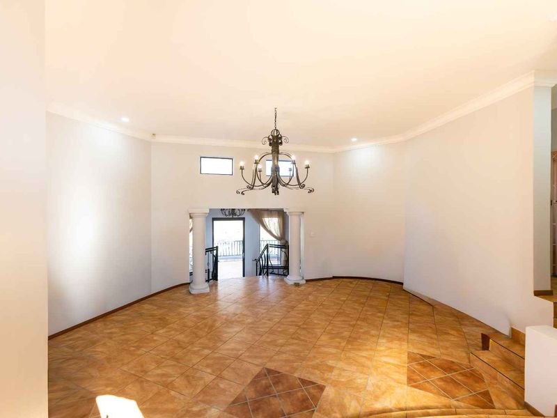 Spacious, light-filled living area featuring tiled flooring, decorative columns, and a classic wrought iron chandelier, offering a versatile open-plan layout.