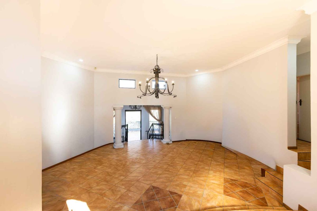 Spacious, light-filled living area featuring tiled flooring, decorative columns, and a classic wrought iron chandelier, offering a versatile open-plan layout.