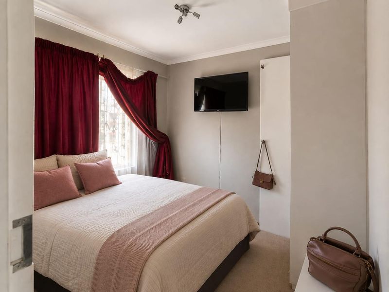 A cozy bedroom featuring neutral wall tones, carpeted flooring, a built-in cupboard, and a wall-mounted television.