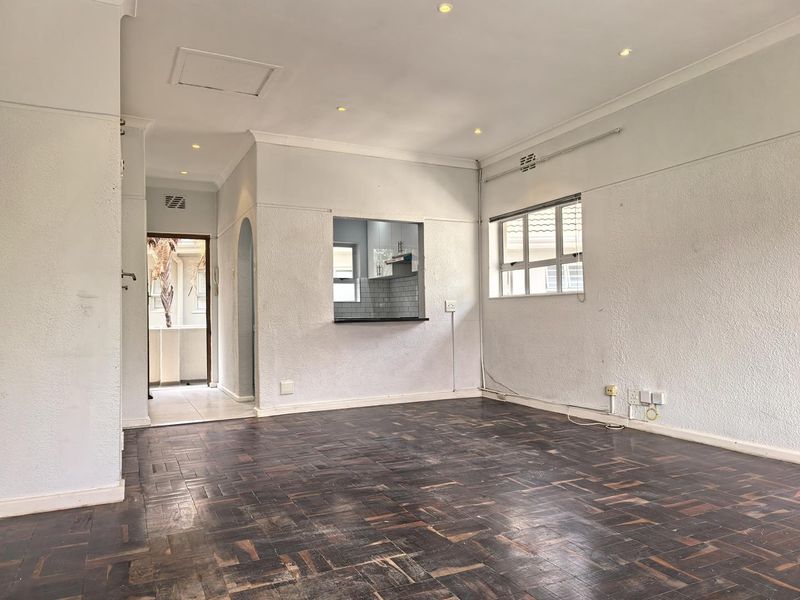 An open-plan living area featuring original parquet flooring, recessed lighting, and a convenient kitchen serving hatch, offering a blank canvas for renovation.