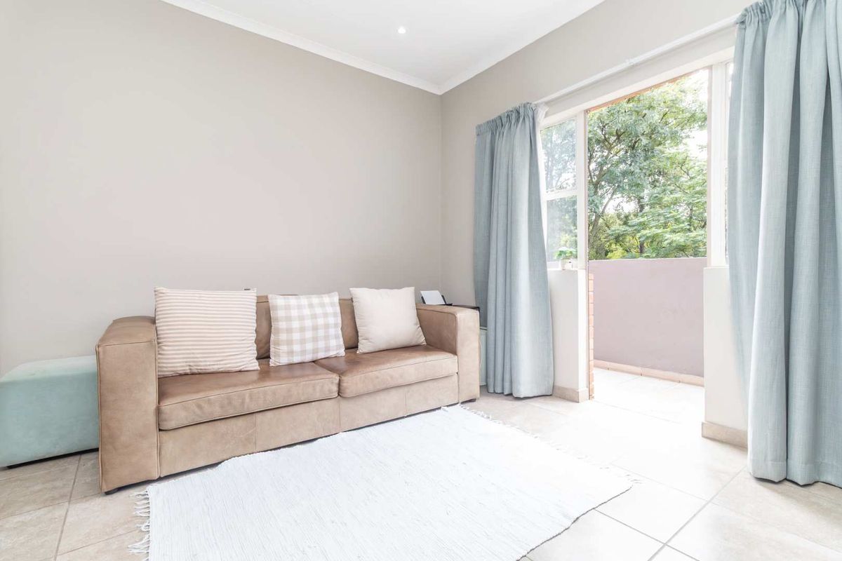 A bright living room featuring neutral tiled flooring and direct access to a private balcony through a large glass door.