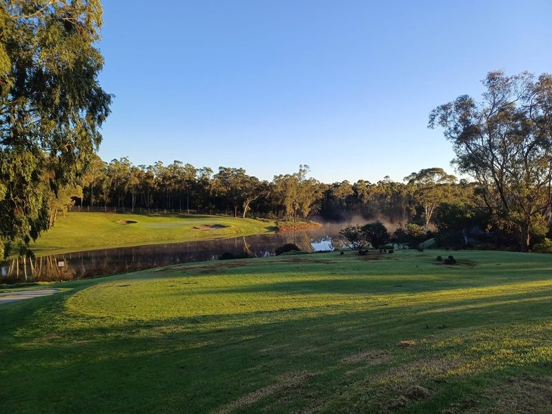 A scenic view overlooking a tranquil lake and manicured golf course fairways, surrounded by mature trees and natural landscape.
