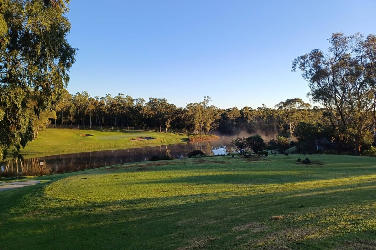 A scenic view overlooking a tranquil lake and manicured golf course fairways, surrounded by mature trees and natural landscape.