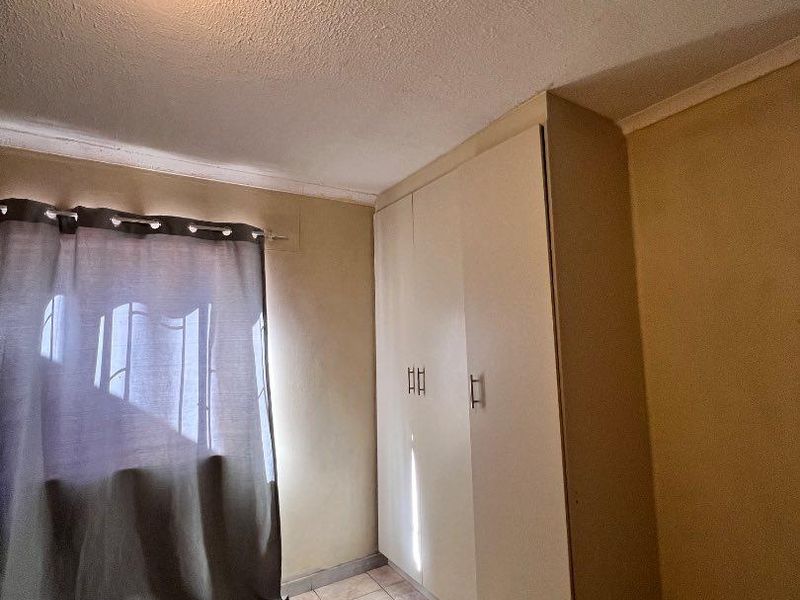 A bedroom featuring tiled flooring and built-in cupboards, requiring cosmetic updates to the walls and ceiling to improve its overall appeal.