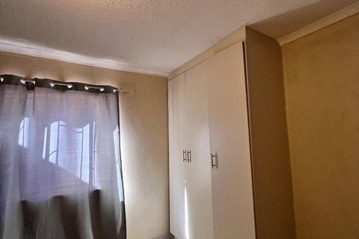A bedroom featuring tiled flooring and built-in cupboards, requiring cosmetic updates to the walls and ceiling to improve its overall appeal.