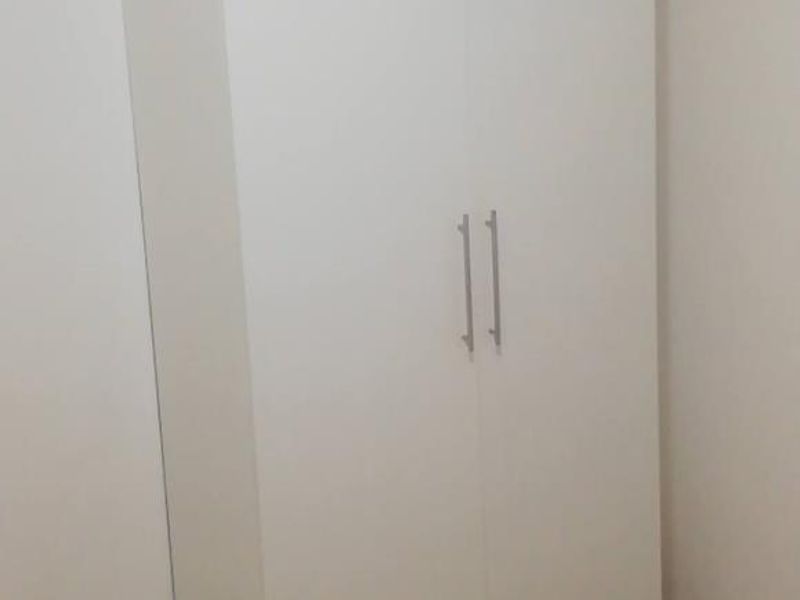 A clean, minimalist bedroom featuring a modern white built-in wardrobe with sleek metal handles.