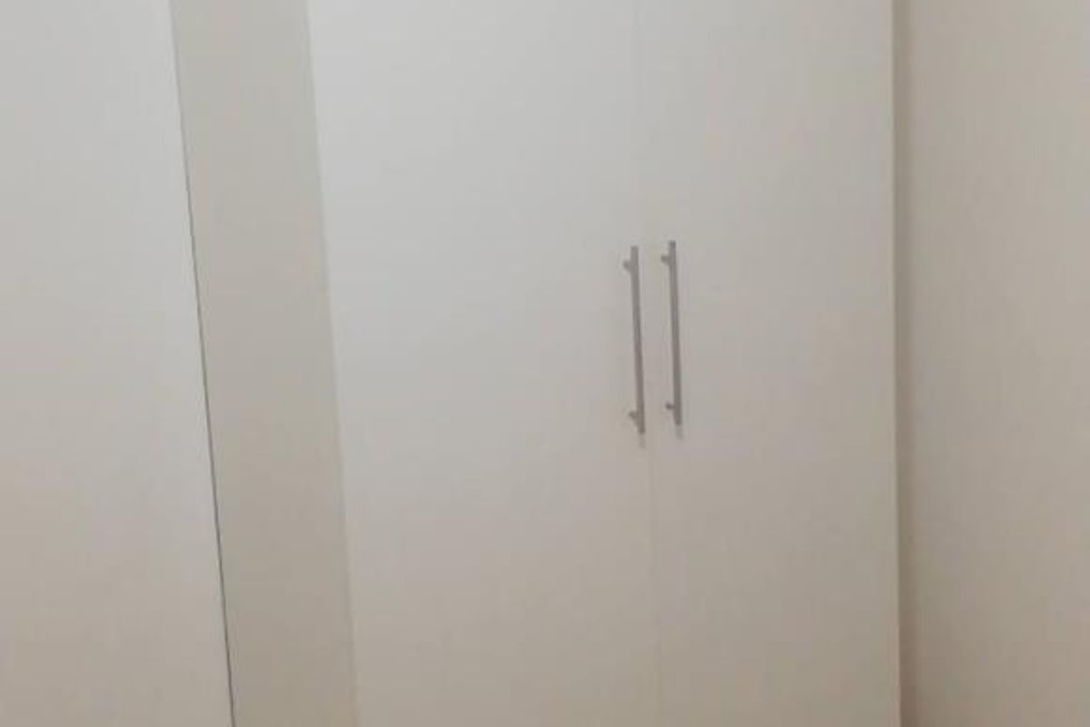 A clean, minimalist bedroom featuring a modern white built-in wardrobe with sleek metal handles.