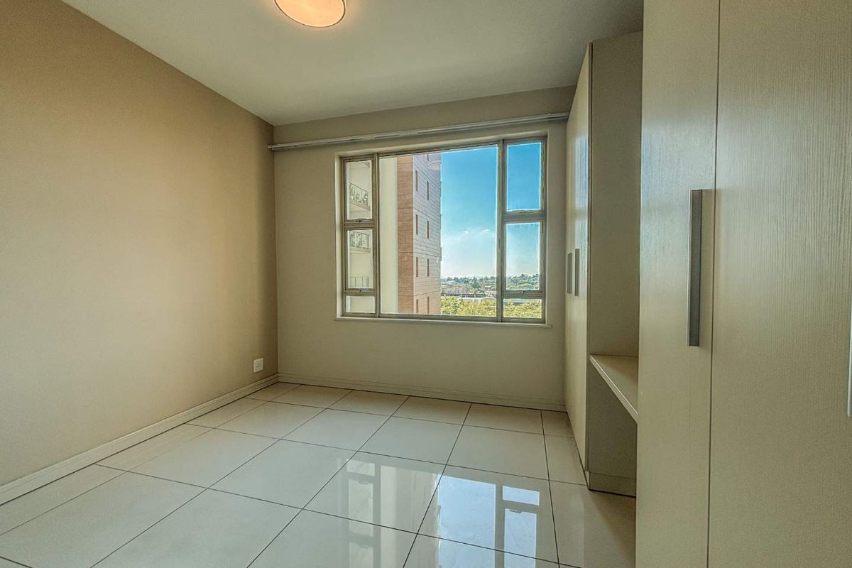 A bright, empty bedroom featuring large windows with a view, tiled flooring, and built-in cabinetry with an integrated desk space.