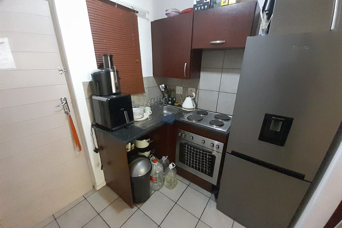Compact kitchen featuring dark wood cabinetry, built-in electric oven and hob, tiled flooring, and a functional layout suitable for an apartment setting.