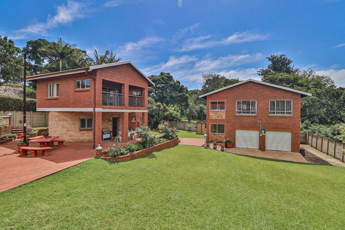 Spacious rear exterior view featuring a two-story face brick house, a separate double garage building, a paved patio area, and a well-maintained garden.