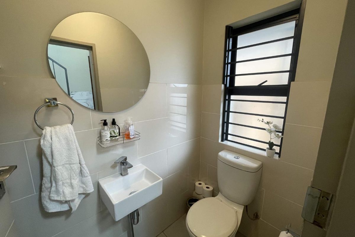 A compact guest bathroom featuring a wall-mounted basin, a modern toilet, and a circular mirror with neutral wall tiling.