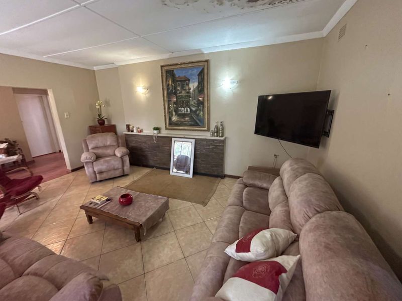 Spacious living room featuring tiled flooring and decorative stone wall cladding, currently showing visible water damage on the ceiling requiring repair.
