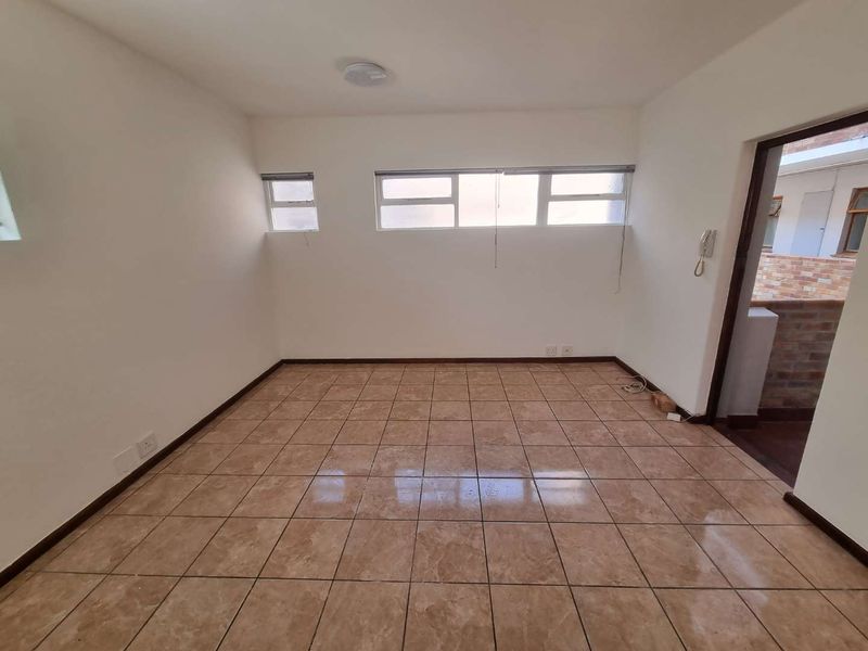 An empty, well-lit living area featuring neutral tiled flooring and high-set horizontal windows, providing a clean and versatile space for customization.