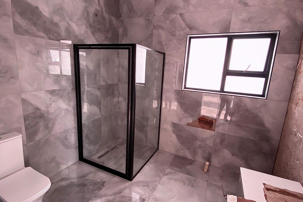 Modern bathroom featuring large-format grey marble-look tiles, a glass shower enclosure with black framing, and a white toilet.