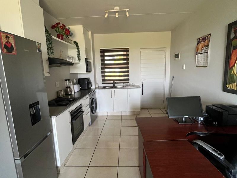 A functional kitchen featuring white cabinetry, tiled flooring, built-in oven and hob, and a stainless steel sink with a window view.