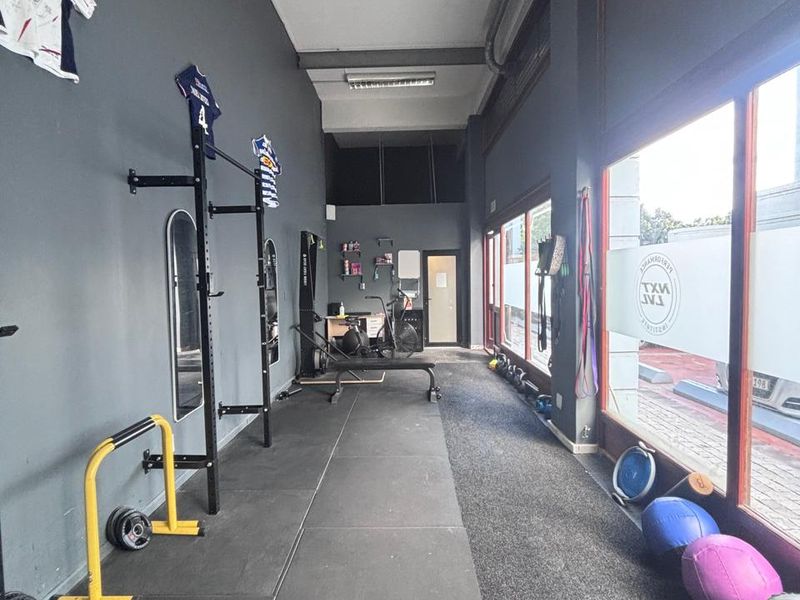 A functional retail gym space featuring durable rubber flooring, large street-facing glass windows, and exposed industrial ceiling elements.