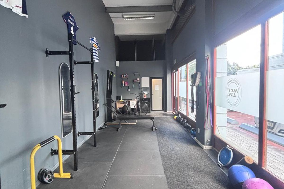 A functional retail gym space featuring durable rubber flooring, large street-facing glass windows, and exposed industrial ceiling elements.