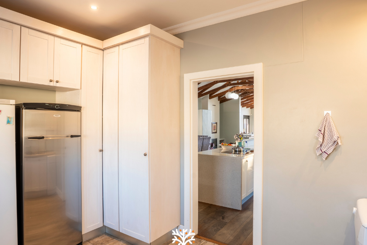 A clean kitchen area featuring light-toned built-in cabinetry, tiled flooring, and crown molding, with a doorway leading into an adjacent living space.