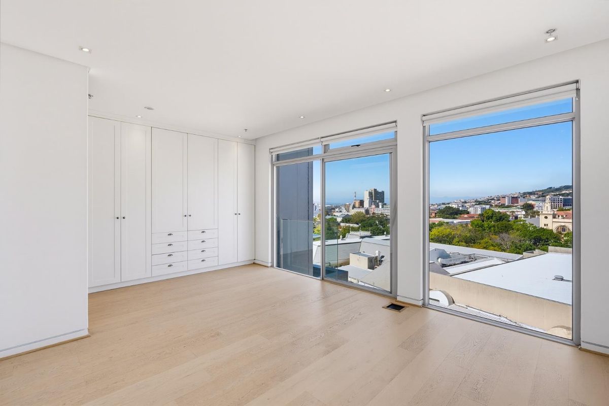 A bright, modern bedroom featuring light hardwood flooring, extensive built-in cabinetry, and large sliding glass doors offering expansive city and landscape views.