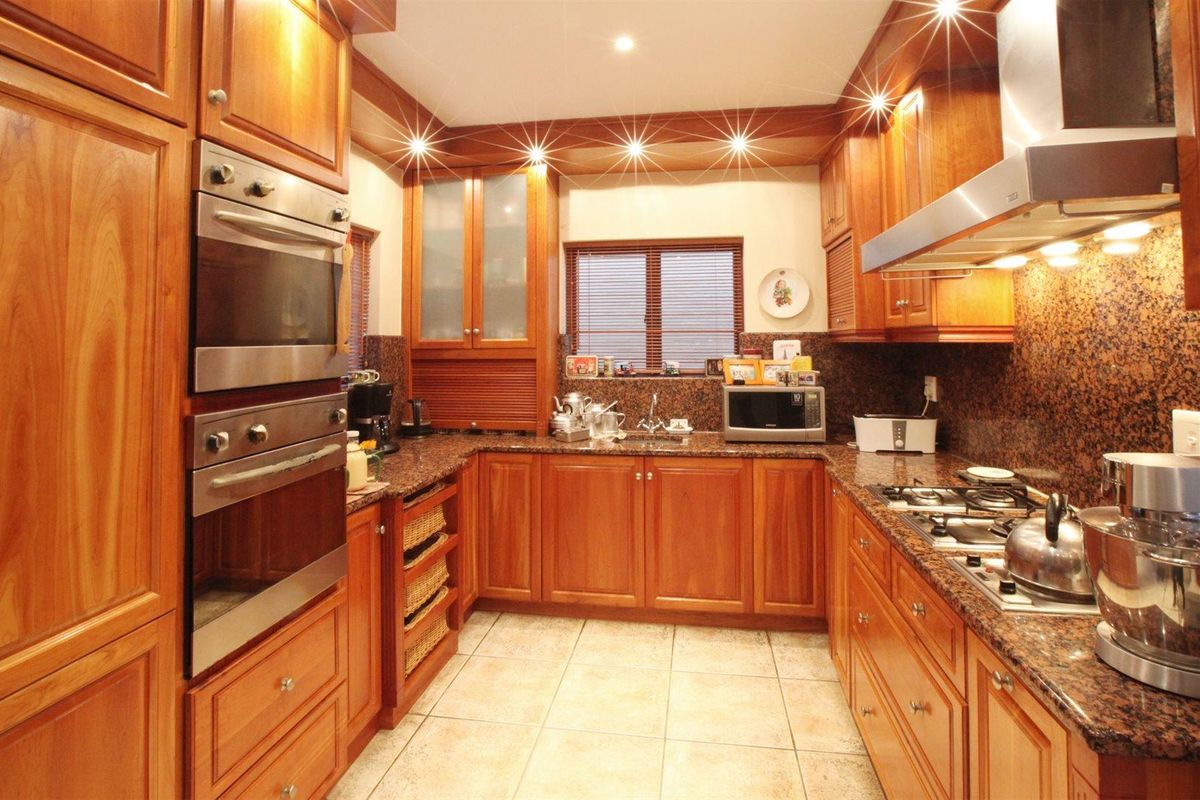 A well-maintained kitchen featuring warm timber cabinetry, granite countertops, a built-in double oven, gas hob, and stainless steel extractor fan.