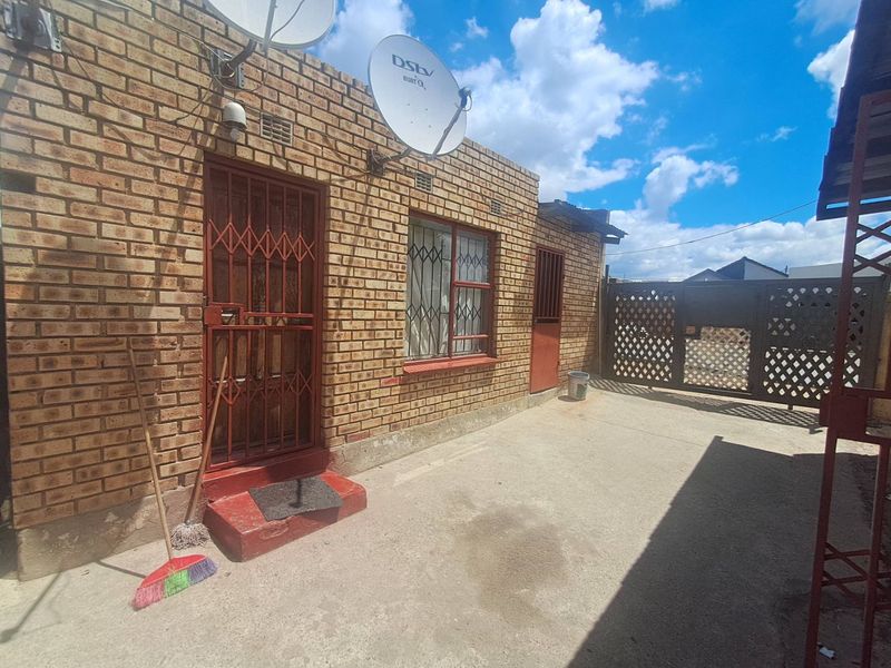 Rear exterior view of a face brick house featuring a paved courtyard, security gates, and security bars on the windows.