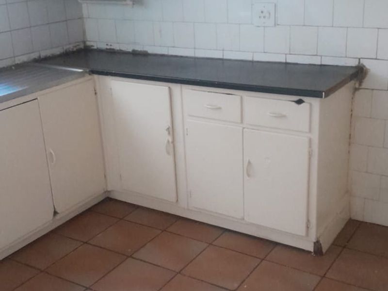 A dated kitchen featuring white built-in cabinetry, tiled backsplash, and tiled flooring, requiring cosmetic updates to modernize the space.