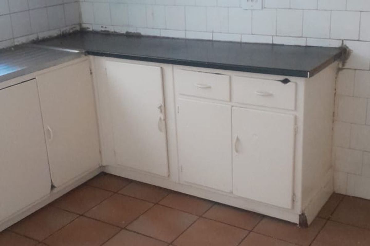 A dated kitchen featuring white built-in cabinetry, tiled backsplash, and tiled flooring, requiring cosmetic updates to modernize the space.