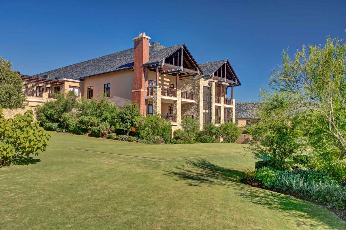A view of the rear elevation of a multi-story apartment building featuring stone cladding, brick chimneys, and timber-framed balconies overlooking a landscaped garden.