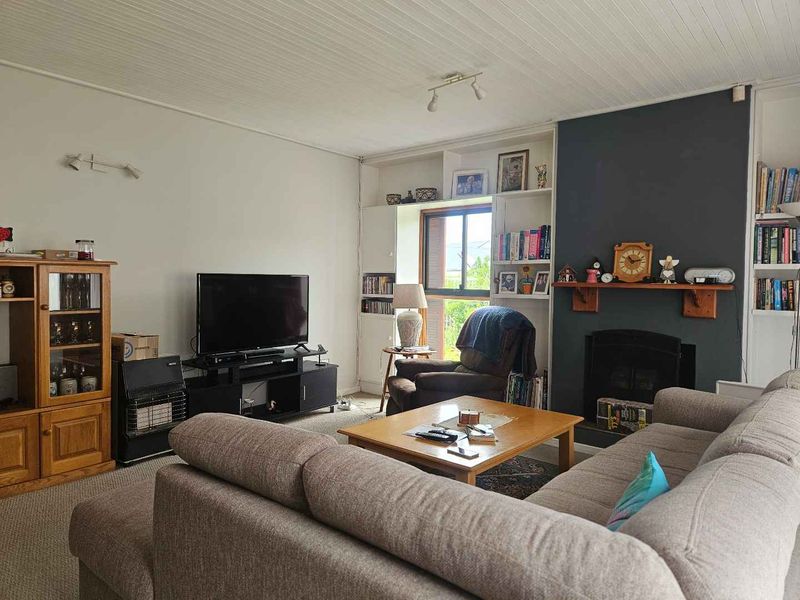 A comfortable living room featuring a fireplace with a timber mantelpiece, built-in shelving, and a classic tongue and groove ceiling.