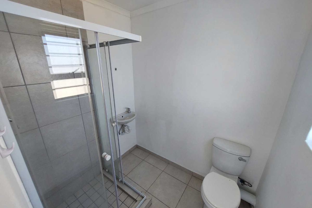A functional bathroom featuring a glass shower enclosure, a wall-mounted basin, and a standard toilet with neutral floor tiling.
