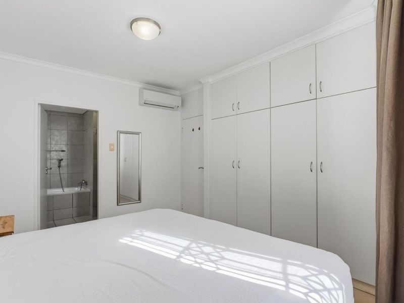 A well-maintained bedroom featuring built-in cupboards, a split-system air conditioner, and direct access to an en-suite bathroom.