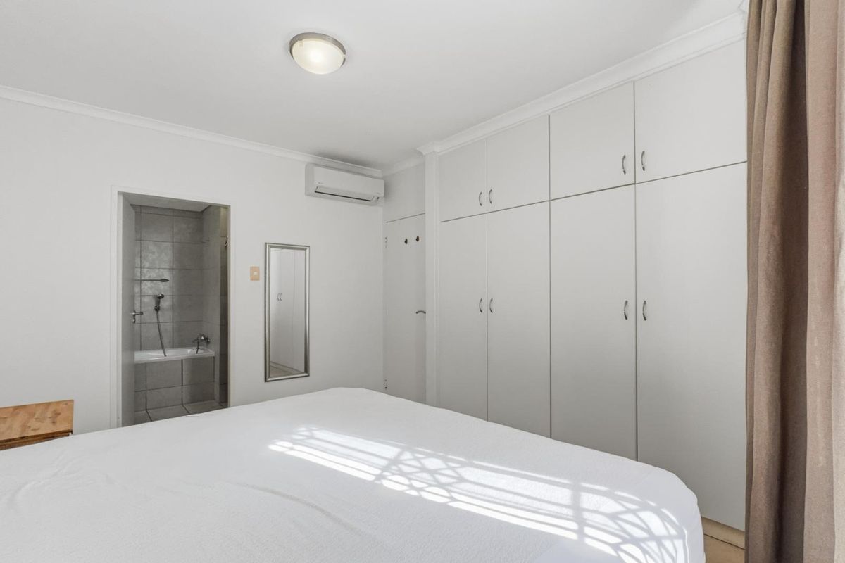 A well-maintained bedroom featuring built-in cupboards, a split-system air conditioner, and direct access to an en-suite bathroom.