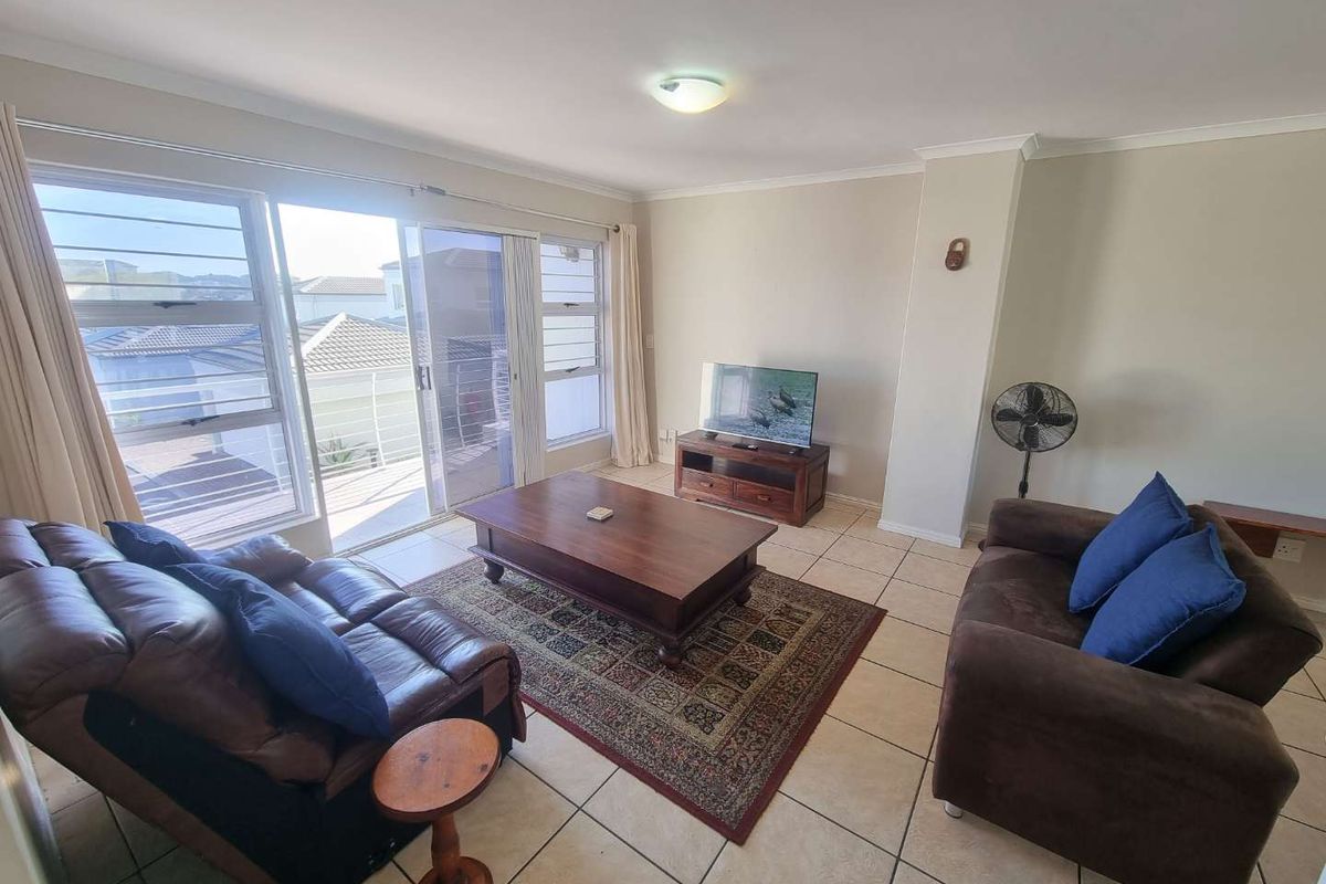 A bright living room featuring tiled flooring and large sliding glass doors that provide access to an outdoor balcony area.