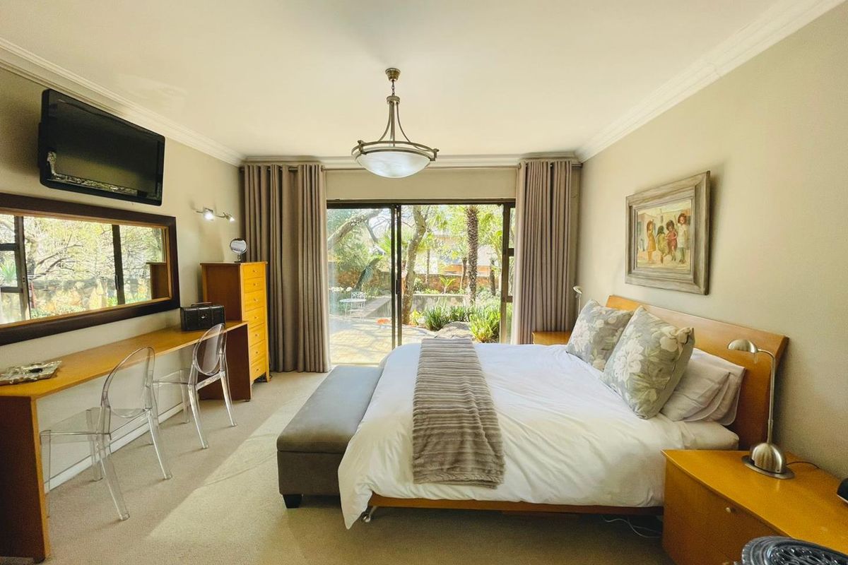 Spacious bedroom featuring neutral carpeting, crown molding, a built-in desk, and sliding glass doors providing direct access to the garden.