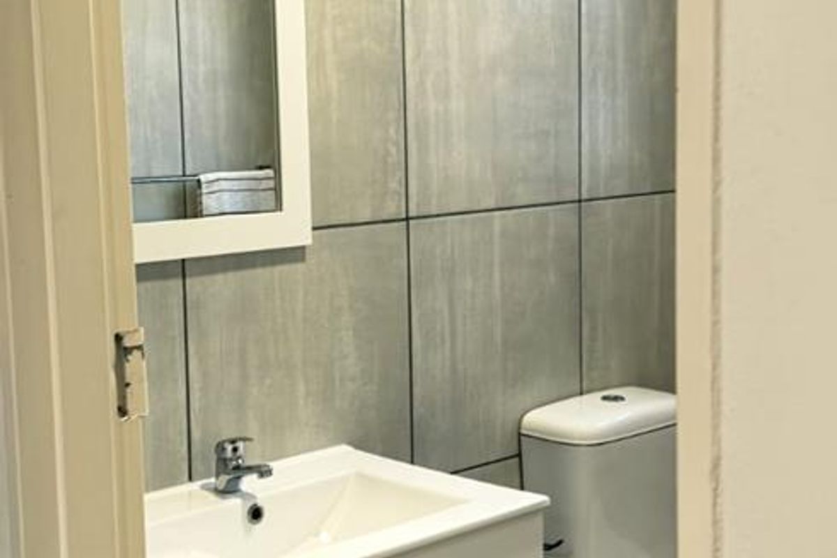 A modern, compact bathroom featuring grey tiled walls and floors, a wall-mounted vanity with a basin, and a standard toilet.