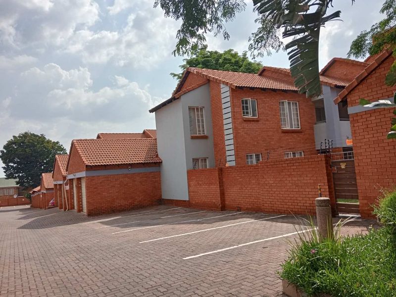 Exterior view of a residential apartment complex featuring red brick facades, tiled roofs, and a paved driveway with designated parking spaces.