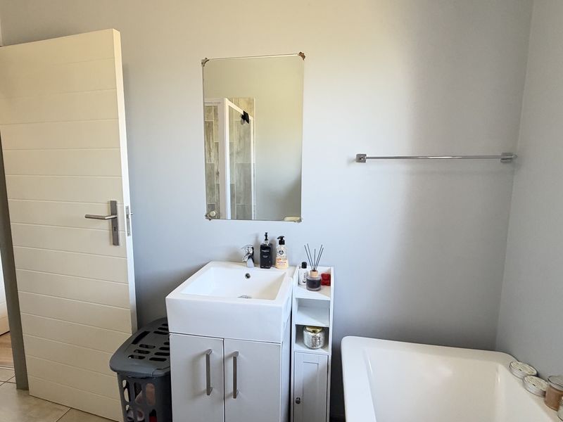 A functional bathroom featuring a modern vanity with basin, wall-mounted mirror, towel rail, and a bathtub with tiled flooring.